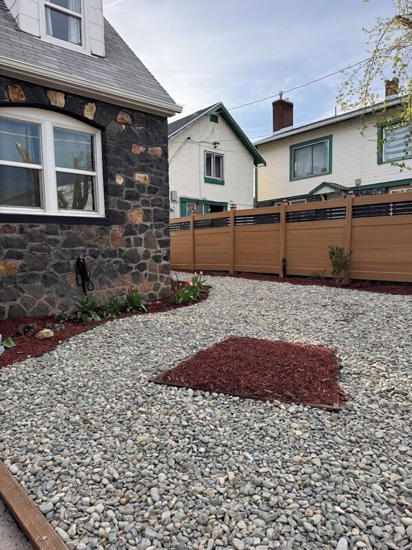 A residential area with a stone house, a wooden fence, and a gravel driveway.