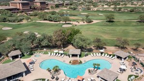 A resort with a large swimming pool, multiple lounge areas, and a golf course in the background.