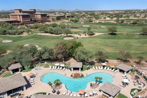 Un complexe hôtelier doté d’une grande piscine, de plusieurs espaces de détente et d’un terrain de golf en arrière-plan.