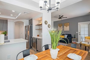 A modern kitchen with a central island, a dining area with a wooden table, and a living room with a dark sofa and decorative wall art.