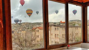 A room with large windows overlooking a cityscape, featuring hot air balloons in the distance. - Yellow Stone Suites (Nevsehir)