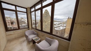 A room with a large window, two armchairs, a small table, and a view of a mountain and buildings. - Yellow Stone Suites (Nevsehir)