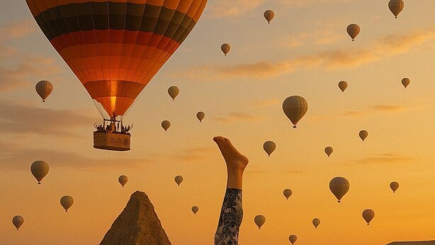 A person performing a handstand on a balcony with a view of hot air balloons and a mountain in the background. - Yellow Stone Suites (Nevsehir)