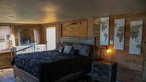 Un dormitorio con una cama grande, paredes de madera, una mesita de noche pequeña y un mapa mundial en la pared.