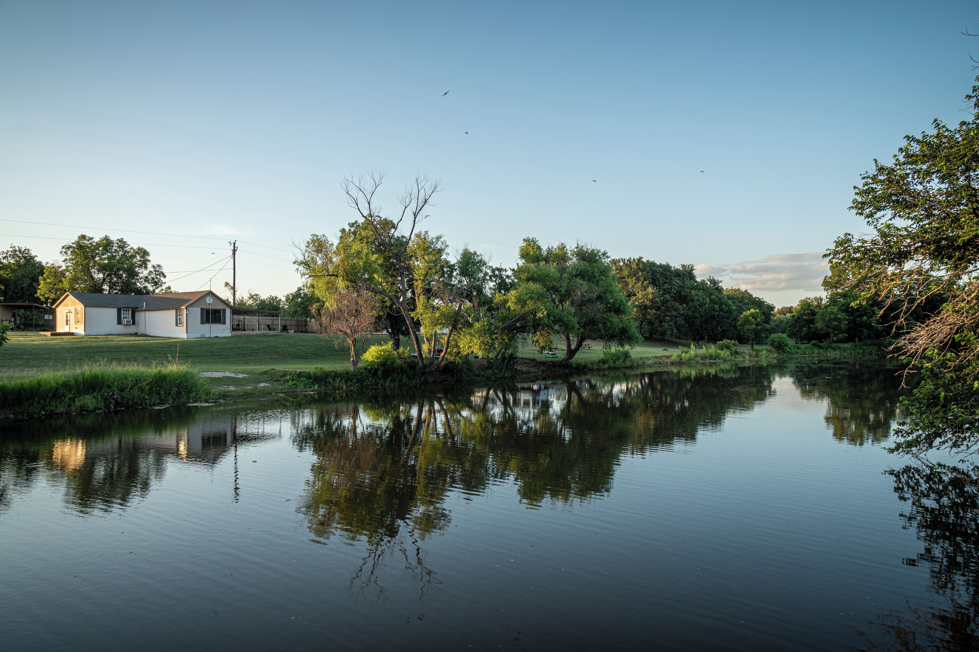 A calm river with reflections of trees and a small building.