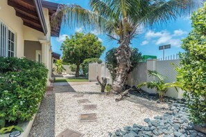 A house with a gravel pathway, palm trees, and a fenced yard.