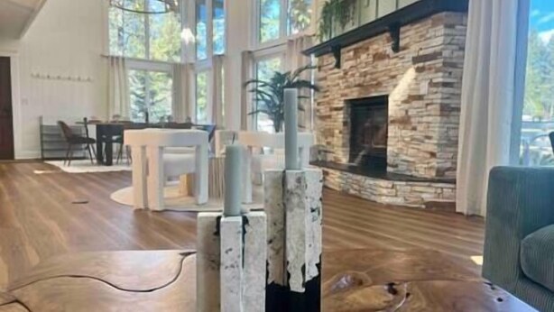 A modern living room with a stone fireplace, wooden flooring, and large windows. - Verde Vista | Steam Shower | Theatre | Hot Tub | Games (East Kootenay)