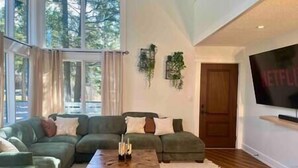 A modern living room with a green sofa, a wooden coffee table, and a large TV on the wall. - Verde Vista | Steam Shower | Theatre | Hot Tub | Games (East Kootenay)