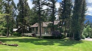 A two-story house with a large front lawn, surrounded by tall trees. - Verde Vista | Steam Shower | Theatre | Hot Tub | Games (East Kootenay)