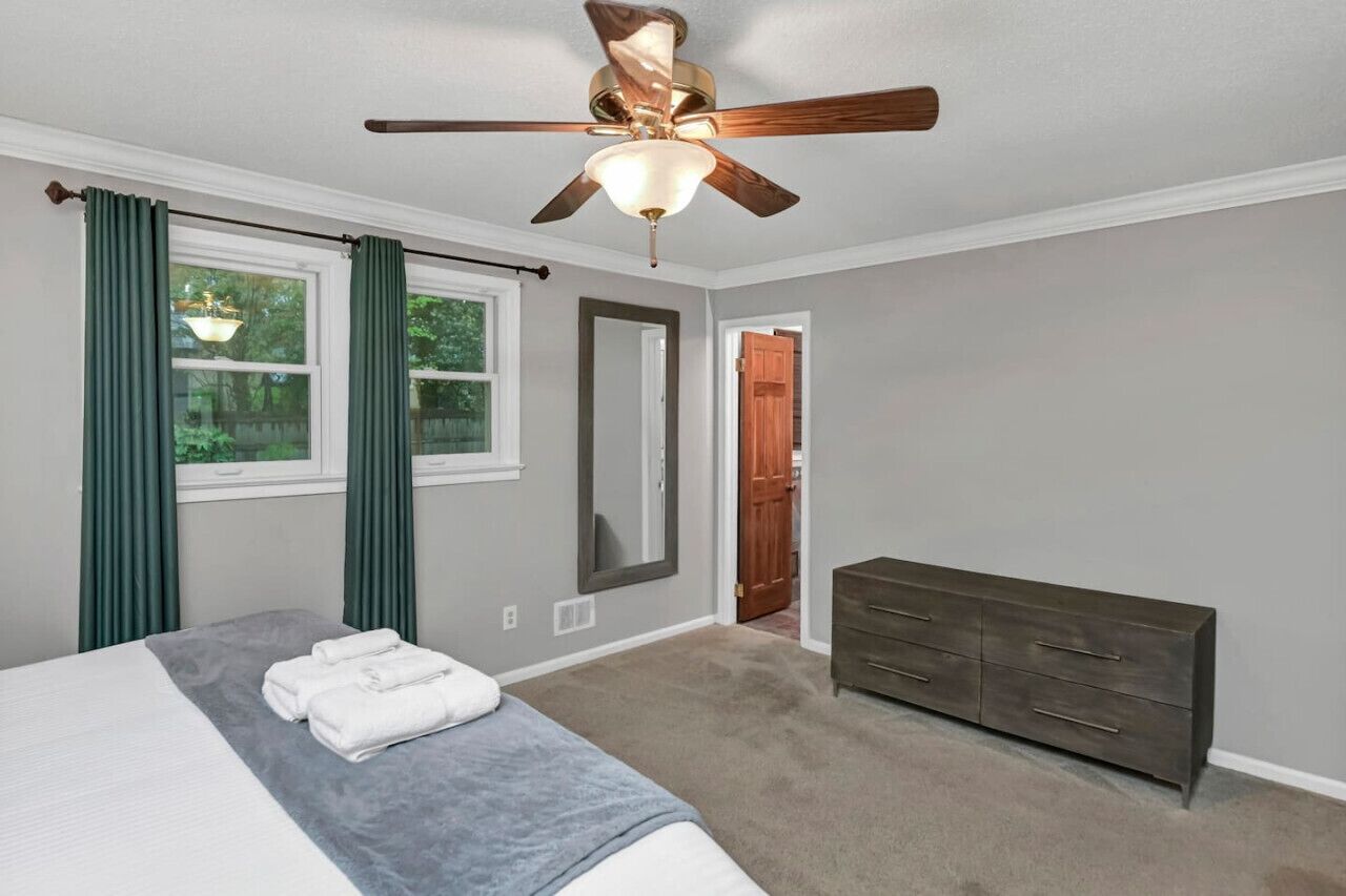 A bedroom with a bed, a dresser, a ceiling fan, and a window with curtains.