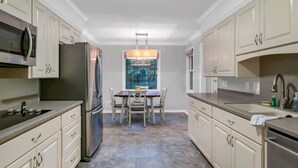 A modern kitchen with light-colored cabinets, stainless steel appliances, and a dining area with a view through a window. - The Quail's Nest of Harbison | Sleeps 8 (Columbia)