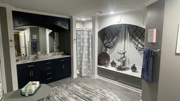 A modern bathroom with a double sink vanity, a shower with patterned curtains, and decorative items on the vanity.