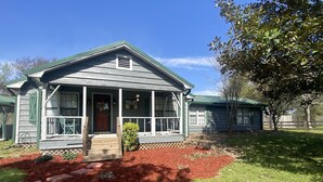 A two-story house with a porch, a small front yard with red mulch, and a wooden fence in the background.