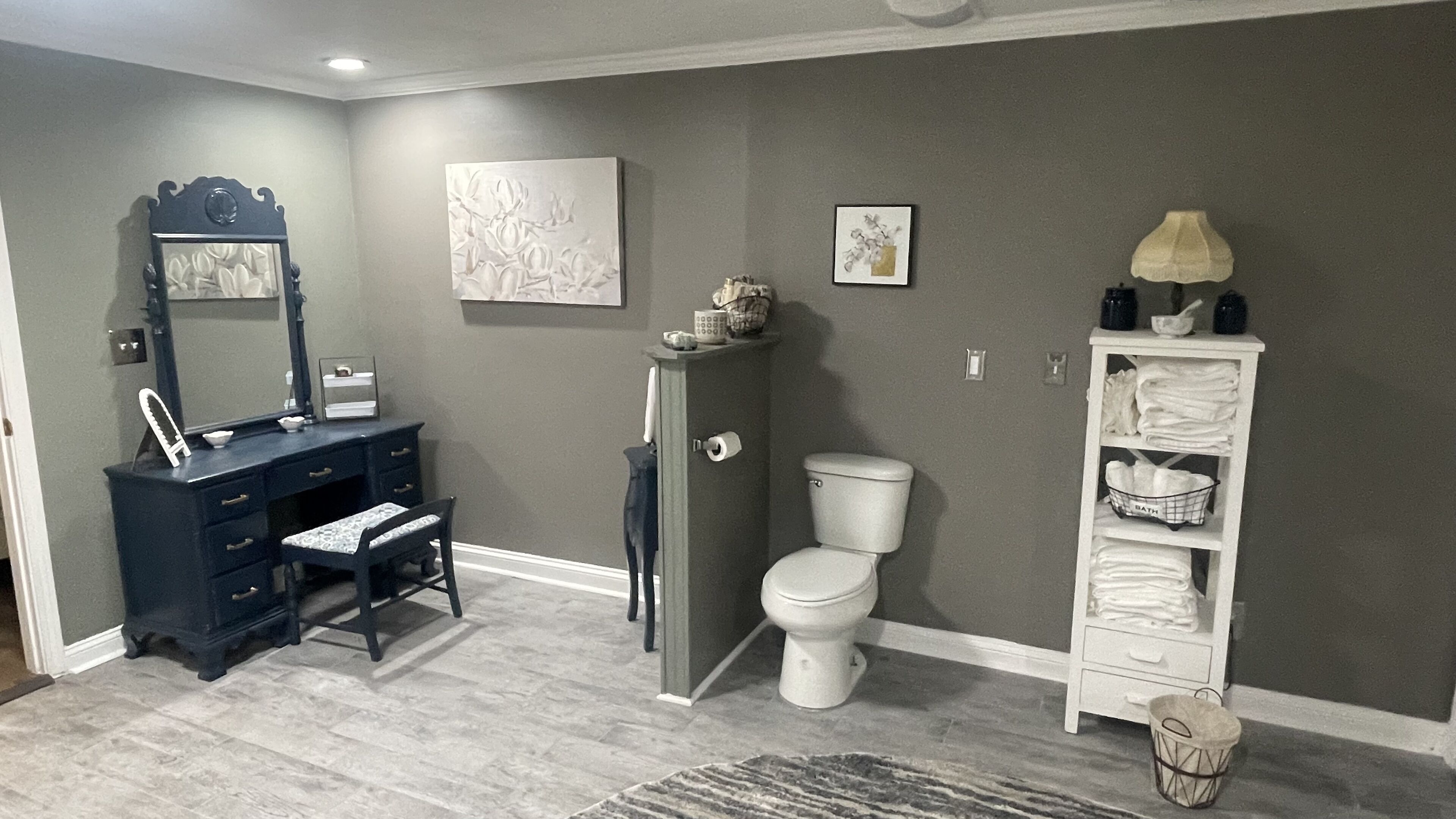 A bathroom with a dark blue vanity, a white toilet, and a white shelving unit with towels.