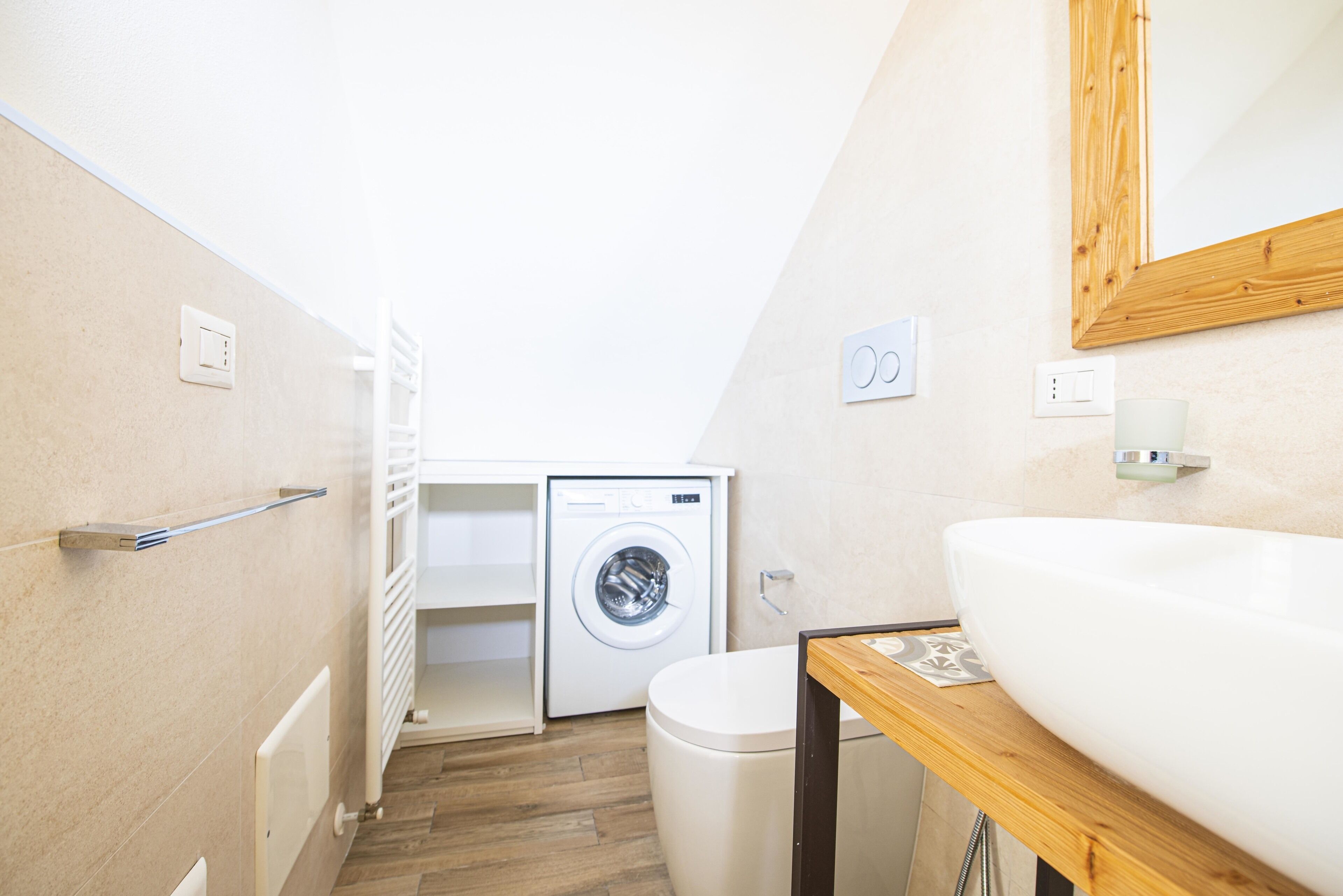 A compact bathroom with a washing machine, a sink, and a wooden countertop.