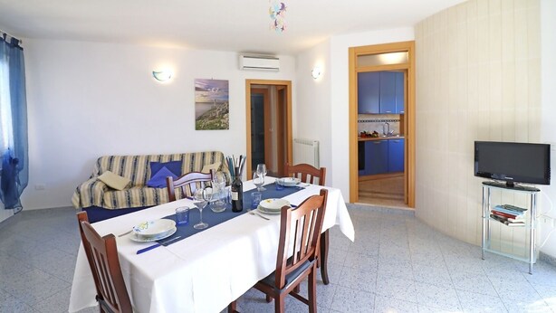 A dining area with a table set for two, a sofa, a television, and a kitchen visible through an open door. - Casa Kris in the center of Otranto (Otranto)
