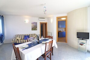 A dining area with a table set for two, a sofa, a television, and a kitchen visible through an open door. - Casa Kris in the center of Otranto (Otranto)