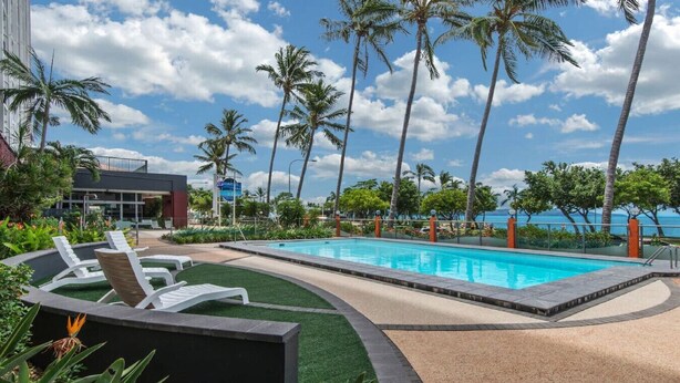 A pool area with lounge chairs, palm trees, and a view of the ocean. - Studio 211-seaside Serenity: Your Perfect Retreat (North Ward)