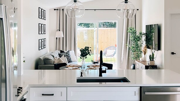 Une cuisine moderne avec des meubles blancs, un lave-vaisselle en acier inoxydable et des luminaires suspendus.