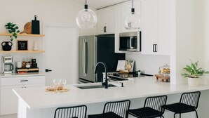 Une cuisine moderne avec des meubles blancs, un îlot central doté de tabourets et des luminaires suspendus.