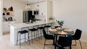 Une cuisine moderne avec un îlot central, des chaises noires et une table à manger pour quatre personnes.