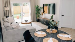 Un salon moderne avec un canapé, une table à manger agrémentée de sets de table, un téléviseur fixé au mur et une porte-fenêtre coulissante donnant sur un espace extérieur.