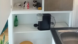 A compact kitchen with white cabinetry, a wooden stool, a coffee maker, and a sink. - Studio 26 m2, à 5 mn de Paris (Arcueil)