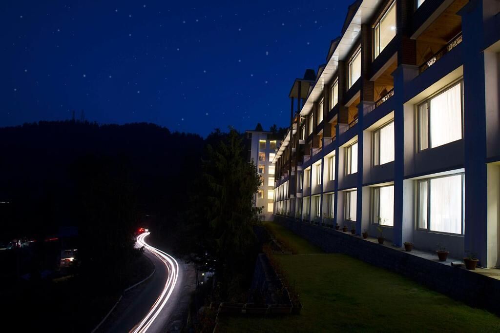 A multi-story hotel with balconies and large windows, a curved road with light trails, and a starry night sky.