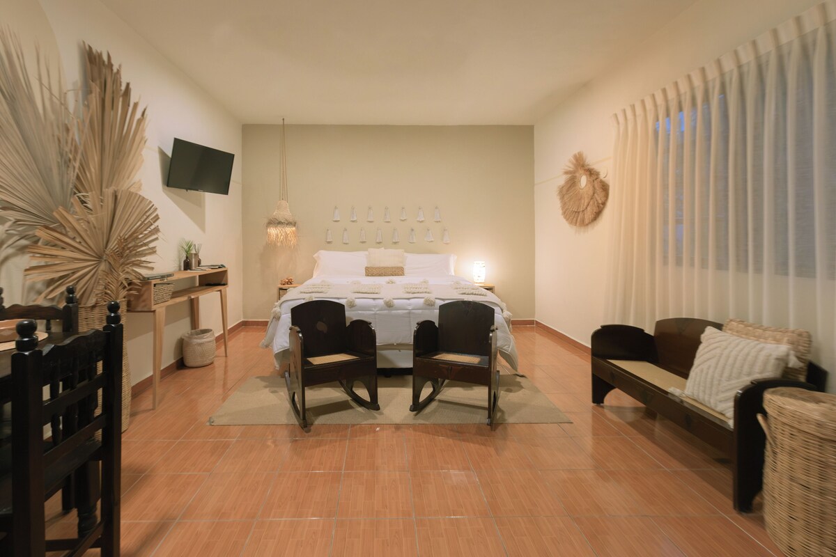 Ein Schlafzimmer mit einem Bett, zwei Stühlen, einem Fernseher und einem Fenster mit Vorhängen.