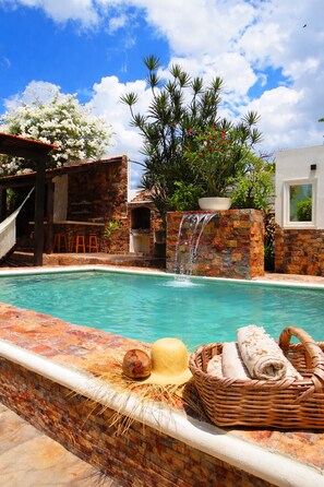 A swimming pool with a waterfall feature, surrounded by stone walls and a wooden pergola. - Casa Magu Merida (Mérida)