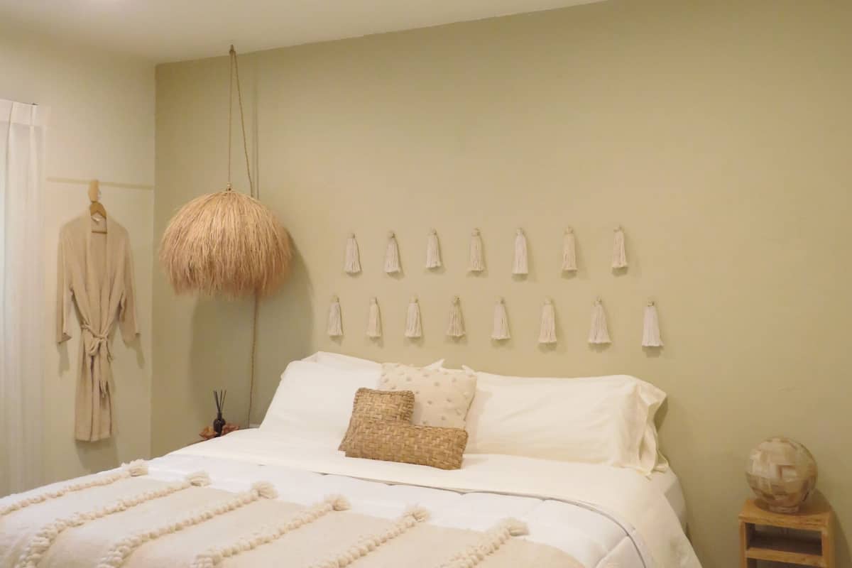 A bedroom with a bed, a hanging light, a wall-mounted towel rack, a wooden stool, and a robe on the wall.