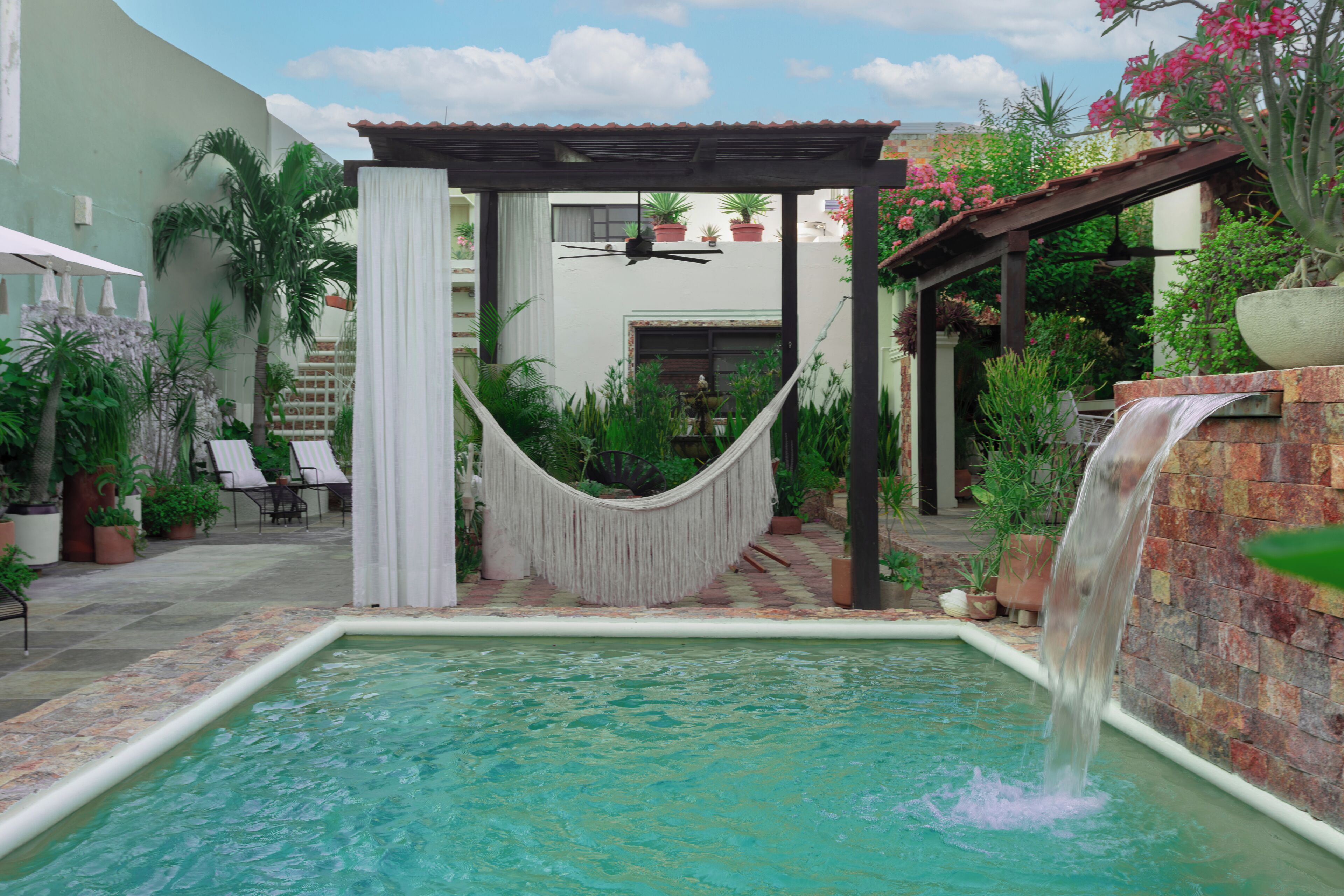 A pool area with a hammock, a small waterfall, and surrounding greenery.