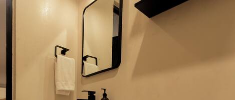 A bathroom with a toilet, a sink, a mirror, and a shelf with a basket.