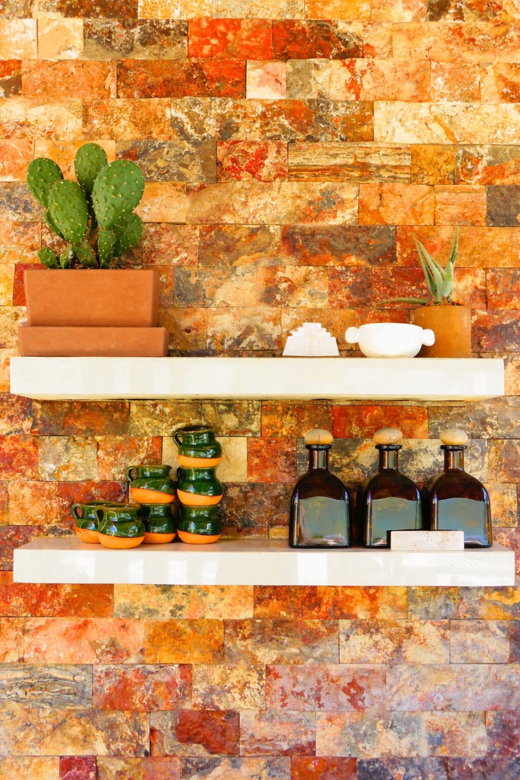 A wall with a mosaic of multicolored tiles, a cactus plant, and shelves with kitchenware.