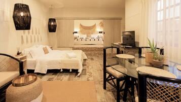 A modern bedroom with a large bed, a dining table with chairs, and a TV.
