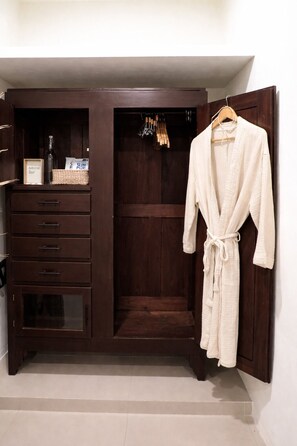 A walk-in closet with a robe hanging, a wooden wardrobe, and a small shelf with items. - Casa Magu Merida (Mérida)