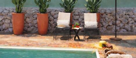 A pool area with chairs, a table, and potted cacti.