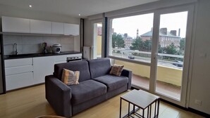 A modern apartment with a grey sofa, a small wooden table, and a kitchen area. - Appartement 4 Personnes à Berck (Berck-sur-Mer)