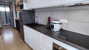 A modern kitchen with white cabinets, a black countertop, a built-in oven, and a coffee maker. - Appartement 4 Personnes à Berck (Berck-sur-Mer)