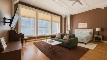 A spacious living room with a piano, a green sofa, a bed, and large windows.
