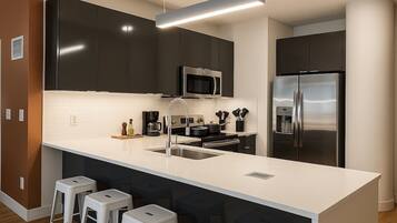 A modern kitchen with dark cabinets, a white countertop, stainless steel appliances, and bar stools.