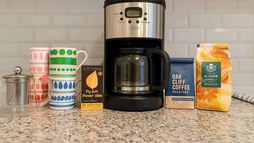 A kitchen counter with a coffee maker, a mug, a coffee pod, and a bag of coffee.