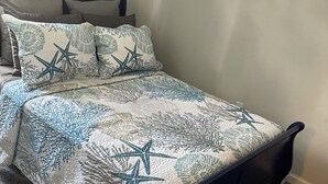 Una cama con un edredón estampado y almohadas, un cabecero oscuro y suelo cubierto de alfombra.