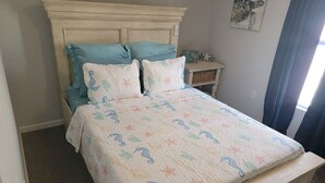 Una cama con colcha que muestra criaturas marinas, un cabecero de madera y una mesita de noche con un adorno.