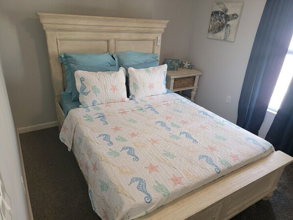 A bed with a quilt featuring sea creatures, a wooden headboard, and a nightstand with a decorative item.