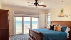 A bedroom with a large bed, a ceiling fan, a view of the ocean through a sliding door, and a star-patterned carpet. - ''Gulls Way'' - Beachfront and Oceanfront Custom Home on Private Beach (Dennis)