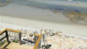 A beach with a wooden walkway leading to a rocky area. - ''Gulls Way'' - Beachfront and Oceanfront Custom Home on Private Beach (Dennis)