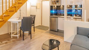 Un salon moderne avec un escalier en bois, un coin repas avec une table et des chaises, et une cuisine équipée d’appareils électroménagers en acier inoxydable.