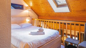 Une chambre avec un plafond en bois, une lucarne, un lit recouvert de draps blancs et une table de chevet.