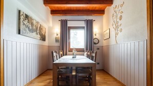 Un coin repas avec une table et des chaises en bois, une fenêtre avec des rideaux, des lampes fixées au mur et un tableau encadré accroché au mur.